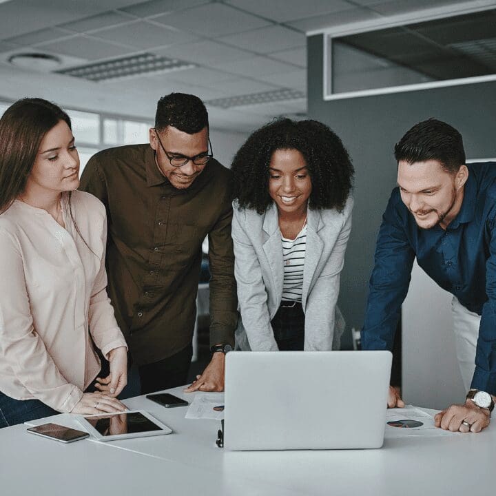 A group of people standing around a table looking at a laptop.